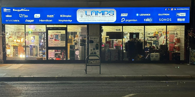 Photo of the LAMPS electrical wholesale branch in Shepherds Bush, London, taken at night with signage and interior lighting visible.